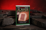 A boxed card deck labeled 'Red Dragon Magic Al Baker Forcing Deck' standing upright on dark slate pieces against a warm red background.