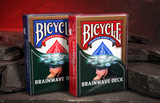 Two Bicycle Brainwave Deck magic tricks standing upright on dark rocks against a glowing red cave background.
