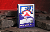 A boxed deck of Bicycle Face Away cards Magic Trick standing upright on dark slate stones against a glowing red cave background.