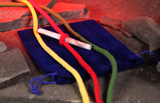 A banknote wrapped in red string, placed on a dark blue velvet pouch with colourful cords in yellow, red, and green resting on gray stones under dramatic red lighting.