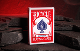 A box of Bicycle Gaff Deck playing cards standing upright on dark stacked stones against a glowing red warm cave background.