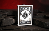 A box of Grey Bicycle Playing Cards on dark slate with a warm red background.