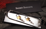 A pair of escapology handcuffs shaped with 2 padlocks with attached keys, displayed in an open black presentation box with a chain, alongside the black lid labelled Houdini's Handcuffs box displayed in a cave with a glowing red background. 