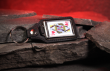 A black leather keyring featuring a playing card design of the Queen of Hearts, resting on dark textured rocks with a glowing red cave background.