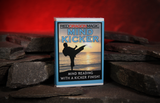 A boxed card deck titled "Mind Kicker" by Red Dragon Magic stands upright on dark stones against a warm red glowing background. The box front shows a silhouette of a martial artist kicking a flying object, with the text "Mind Reading with a Kicker Finish!".