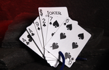 A fan of playing cards, including jokers and aces through sixes of spades, tied with a blue string, displayed on a dark textured surface with a glowing red background.
