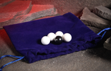 Four white pearls and one black laying on a blue velvet bag on a stone cave floor with a glowing red background. 