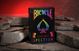 A deck of Bicycle Spectrum Rider Back Playing Cards on a stone floor with a glowing red cave background. 