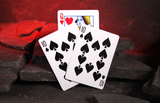 Three playing cards, 10 of spades, 10 of spades, and Queen of hearts, fanned out on dark stones with a red glowing background.